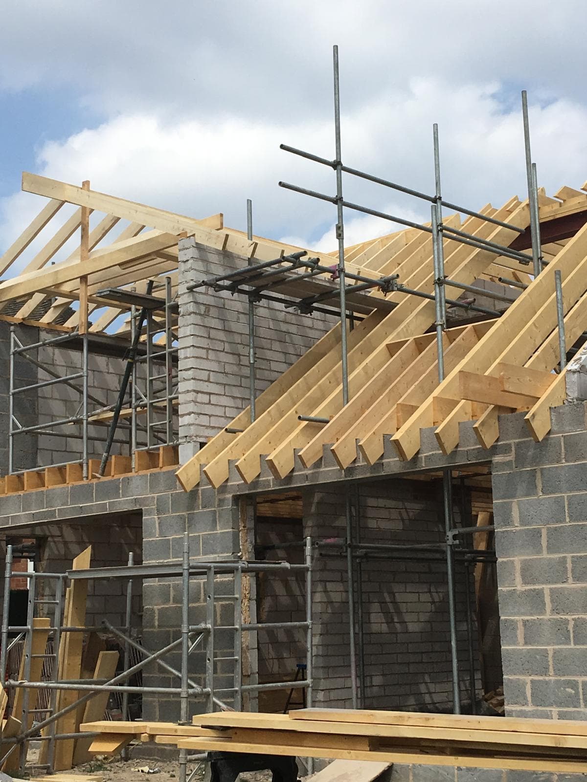 New roof rafters over insulated blockwork gable with reclaimed brick outer leaf, under scaffolding.
