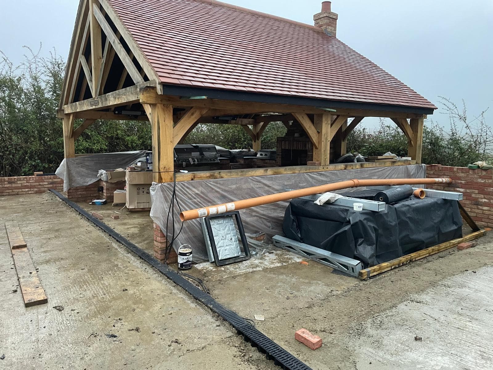 Oak-framed garden pavilion with a tiled roof housing a brick outdoor kitchen.
