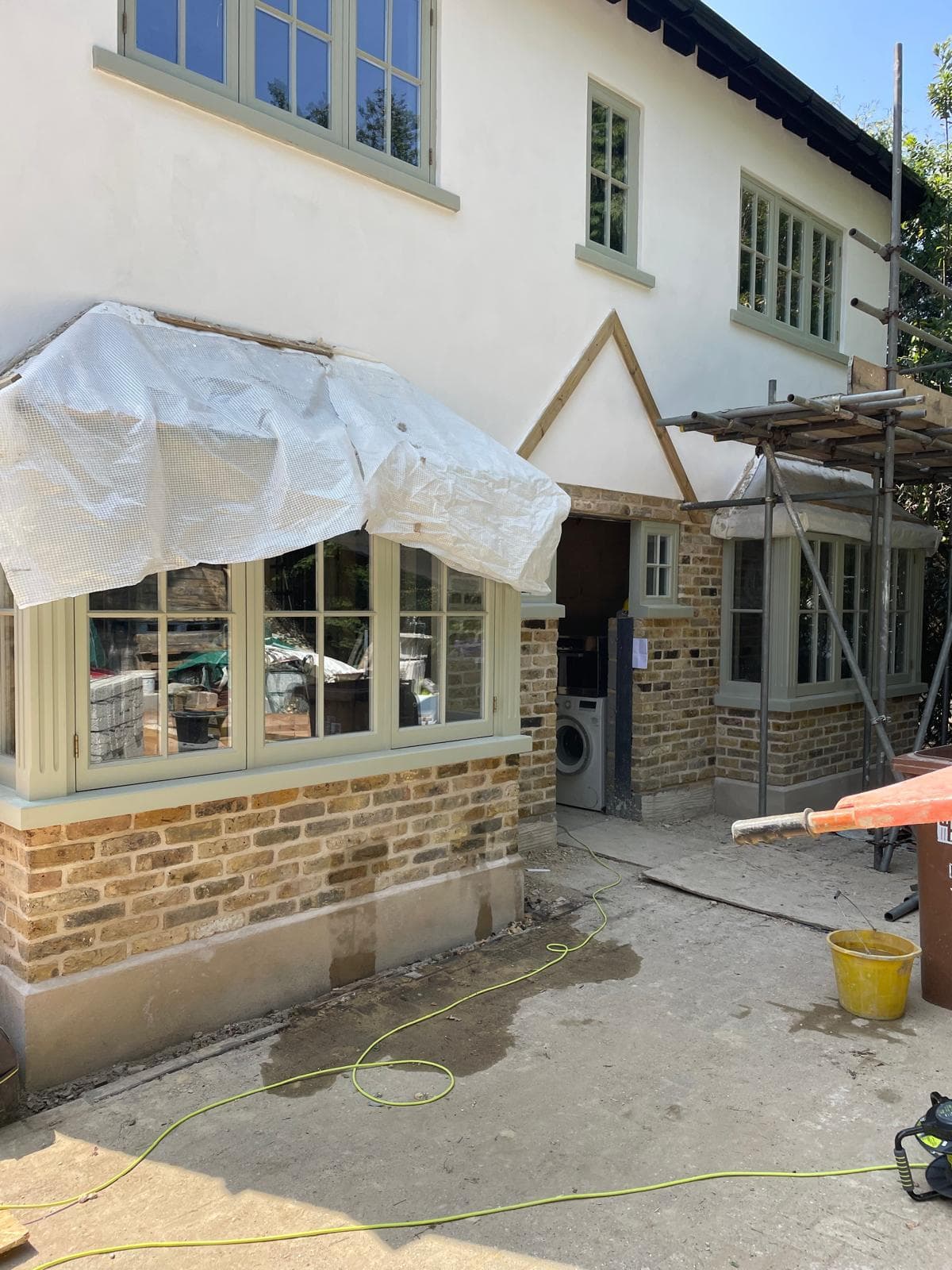 Period property with new sage-green timber bay windows over a reclaimed yellow-stock brick plinth.