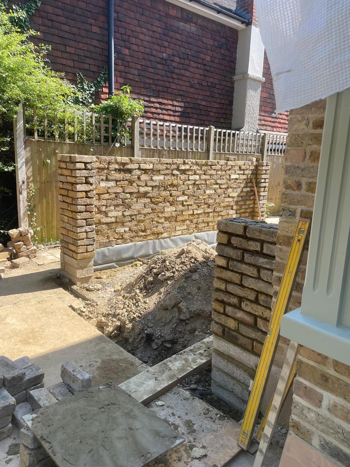 Newly built garden wall in reclaimed yellow-stock brick alongside a period house.