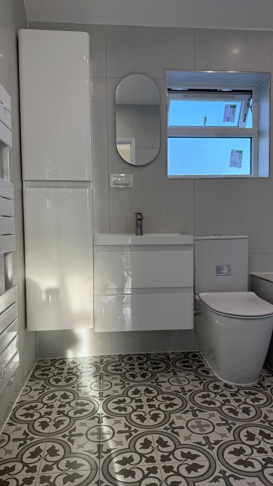 Finished bathroom with patterned encaustic-style floor tiling, wall-hung vanity and tall storage unit.