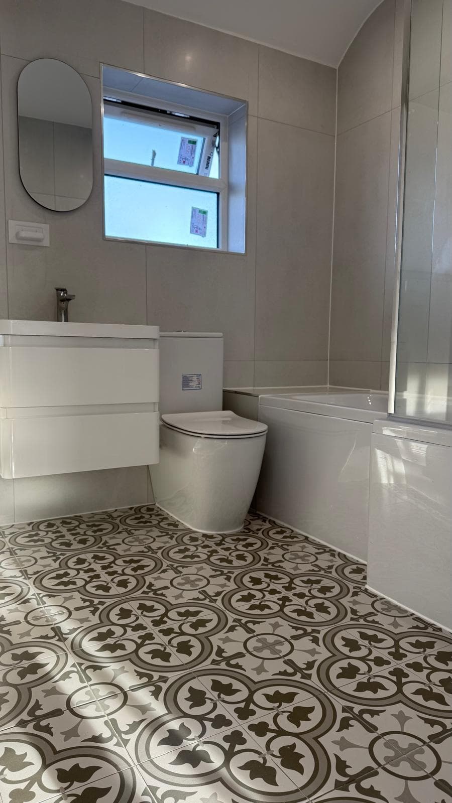 Completed bathroom with wall-hung vanity, back-to-wall WC, bath with shower screen and patterned floor tiles.