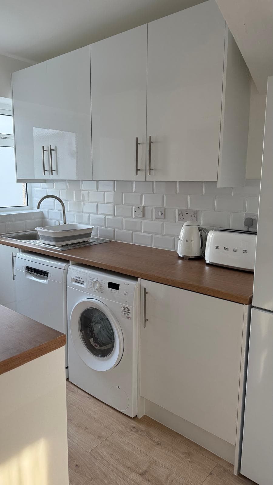 Finished kitchen with gloss white units, oak worktop, metro tile splashback and integrated appliances.